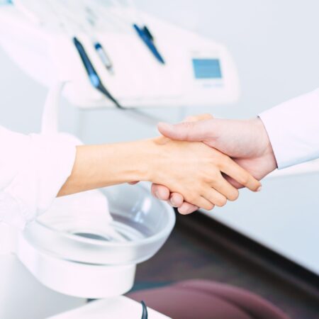 two hands which expressing some kind of bargain made in the dentist room in front of the dentist chair.