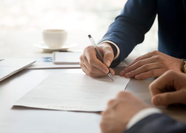 Close up image of businessman hand putting personal signature on contract document in presence of business partner. Starting successful partnership with entrepreneur or companie, making good deal