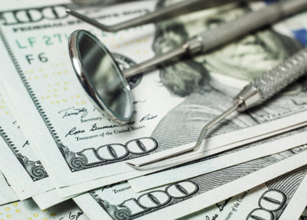 Dental tools mirror, tweezers and a hook on a stack of cash dollar bills. Concept expensive dentistry or dental insurance