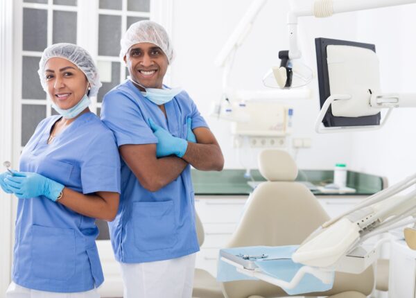 Two professional hispanic dentists in blue uniforms standing back to back in modern office of dental clinic