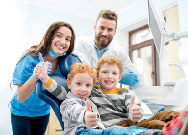 Portrait of happy young boys sitting on the chair with dentist and woman assistant at the dental office