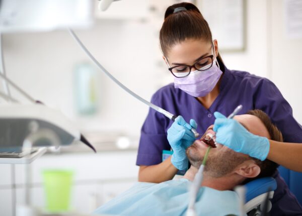 Young female dentist drilling tooth to patient in dental clinic