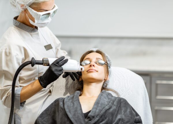 Professional doctor in protective wear making a laser rejuvenation treatment for a young woman client at medical office. LaseMD procedure