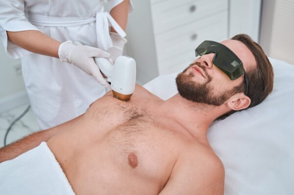 Calm young man in safety goggles lying on the couch during the laser chest hair removal