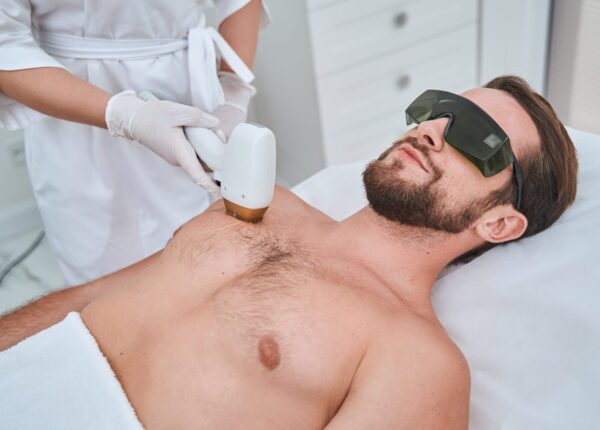 Calm young man in safety goggles lying on the couch during the laser chest hair removal