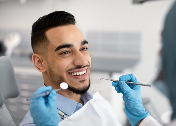 Closeup Of Happy Middle Eastern Male Patient Getting Dental Treatment In Modern Clinic, Islamic Dentist Woman Examining Teeth Of Arab Man With Sterile Tools In Stomatological Cabinet, Cropped Shot