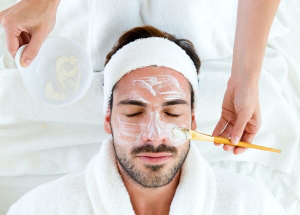 Portrait of man with clay facial mask in beauty spa.