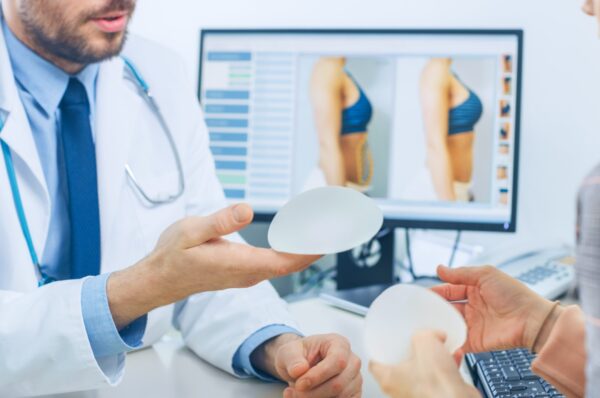 Plastic / Cosmetic Surgeon Shows Female Patient Breast Implant Samples for Her Future Surgery. Professional and Famous Surgeon Working in Respectable Clinic.