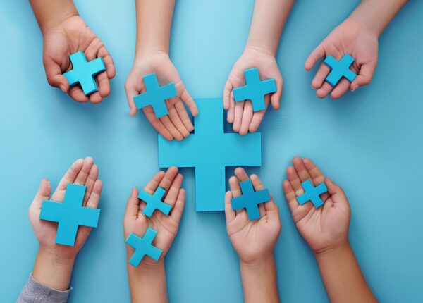 hands holding a red plus sign on a blue background, taken from a top view. The concept represents World Health Day and medical care concepts. A banner with copy space text.