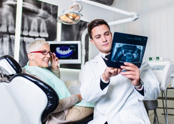 Handsome smiling dentist looking at x-ray image of his senior woman patient.