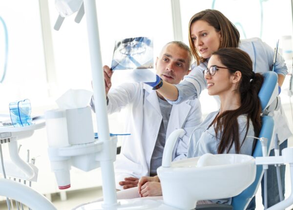 Dentist and his assistant in dental office talking with female patient and preparing for treatment.Examining x-ray image.